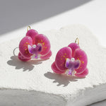 Pink and purple orchid flower earrings with pearl accents, handcrafted resin floral jewelry on light background.