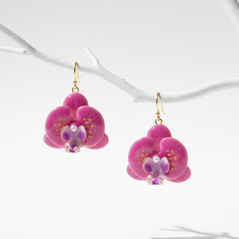 Pink orchid flower drop earrings with purple accents and pearls, handcrafted resin floral jewelry hanging on white branch.