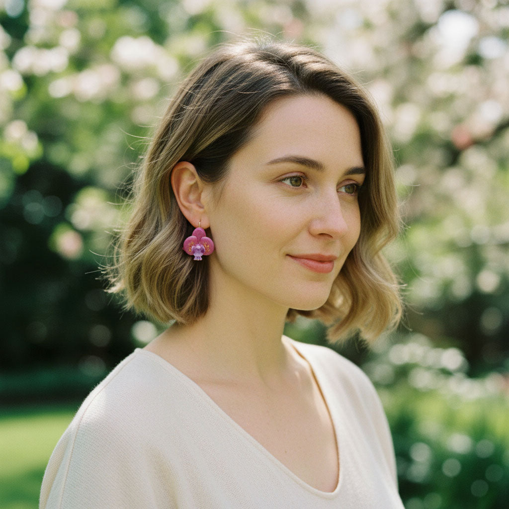 Model wearing pink orchid flower earrings with purple centers and pearl accents, handcrafted resin floral jewelry.