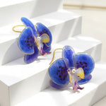 Blue orchid-shaped earrings on a white geometric background