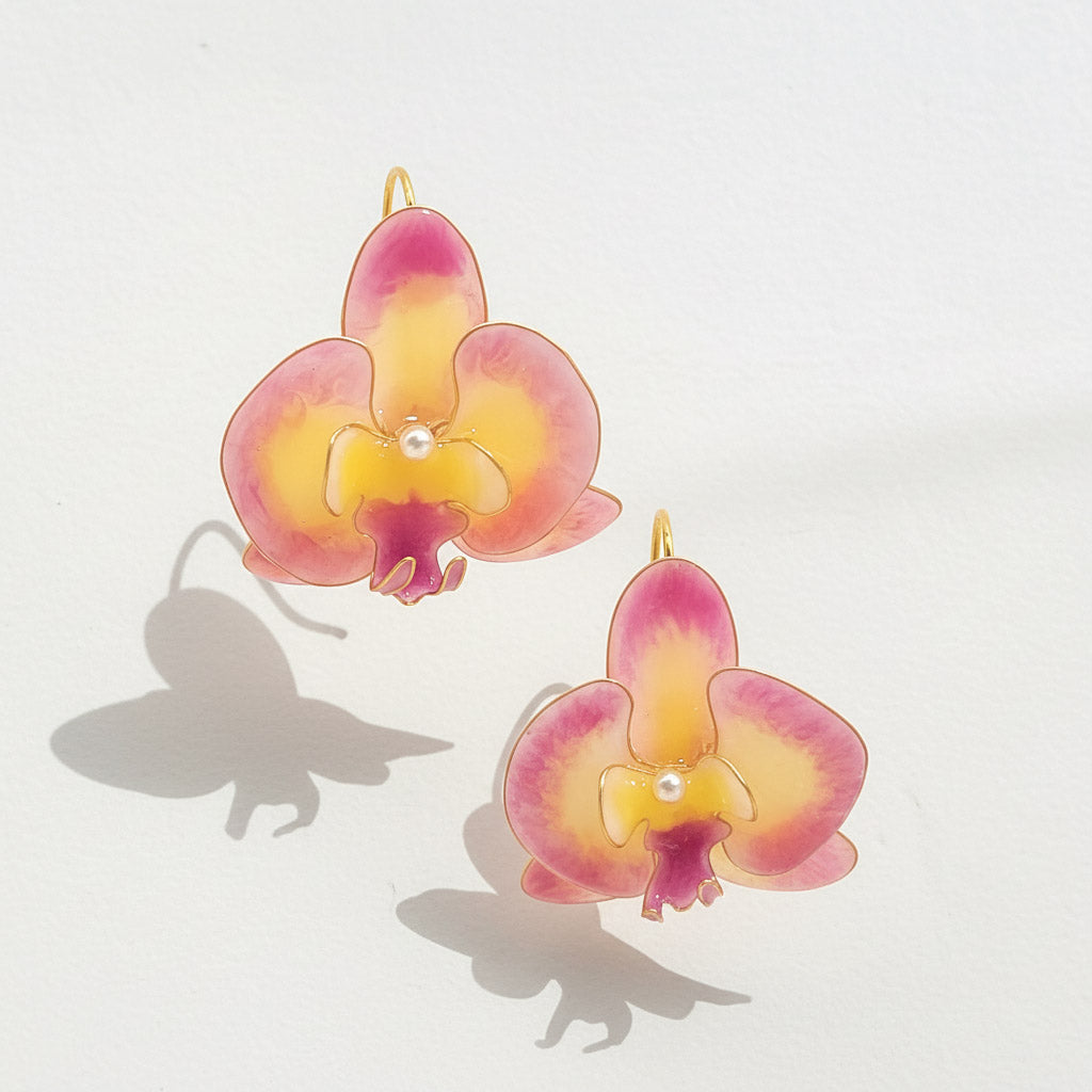 Pair of pink and yellow orchid-shaped earrings on a light gray background