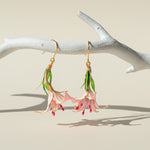 Fairy earrings with pink flowers and green leaves hanging from a branch on a beige background