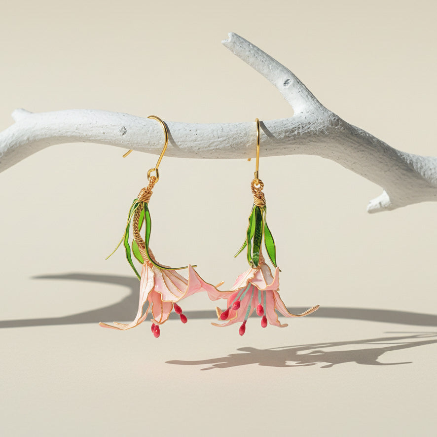 Fairy earrings with pink flowers and green leaves hanging from a branch on a beige background