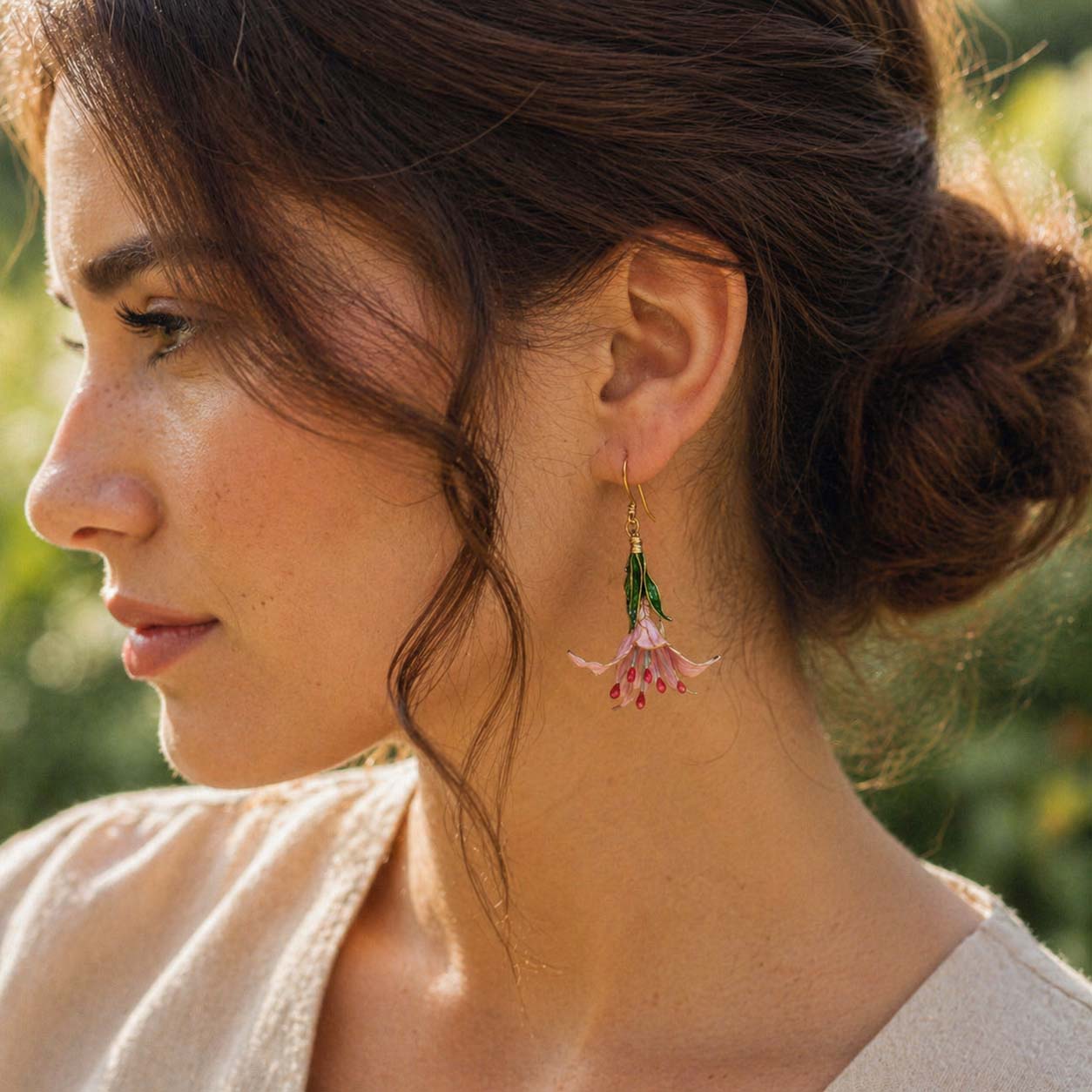 Close-up of a woman wearing hand painted lily earrings with a blurred natural background
