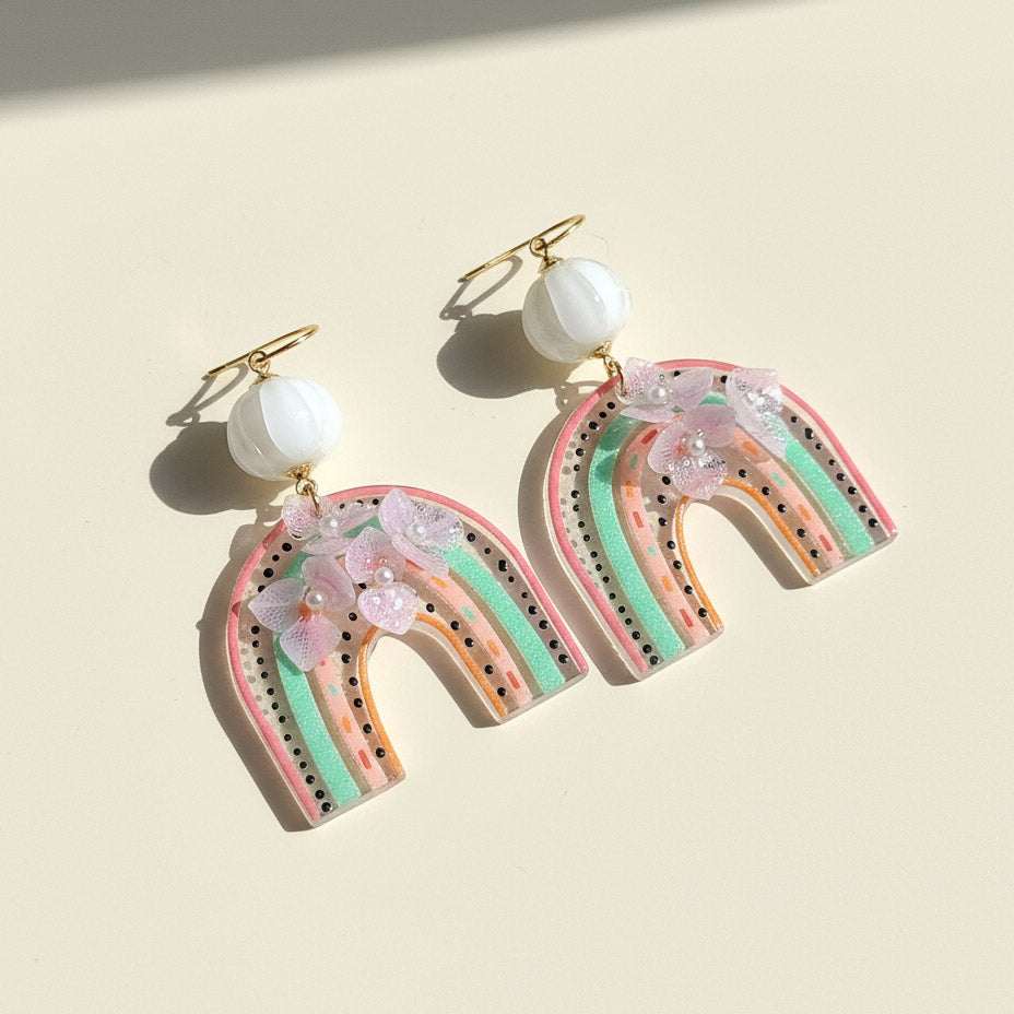 Rainbow-shaped earrings with floral details on a beige background
