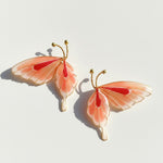 Butterfly-shaped earrings with pink and red wings on a light background