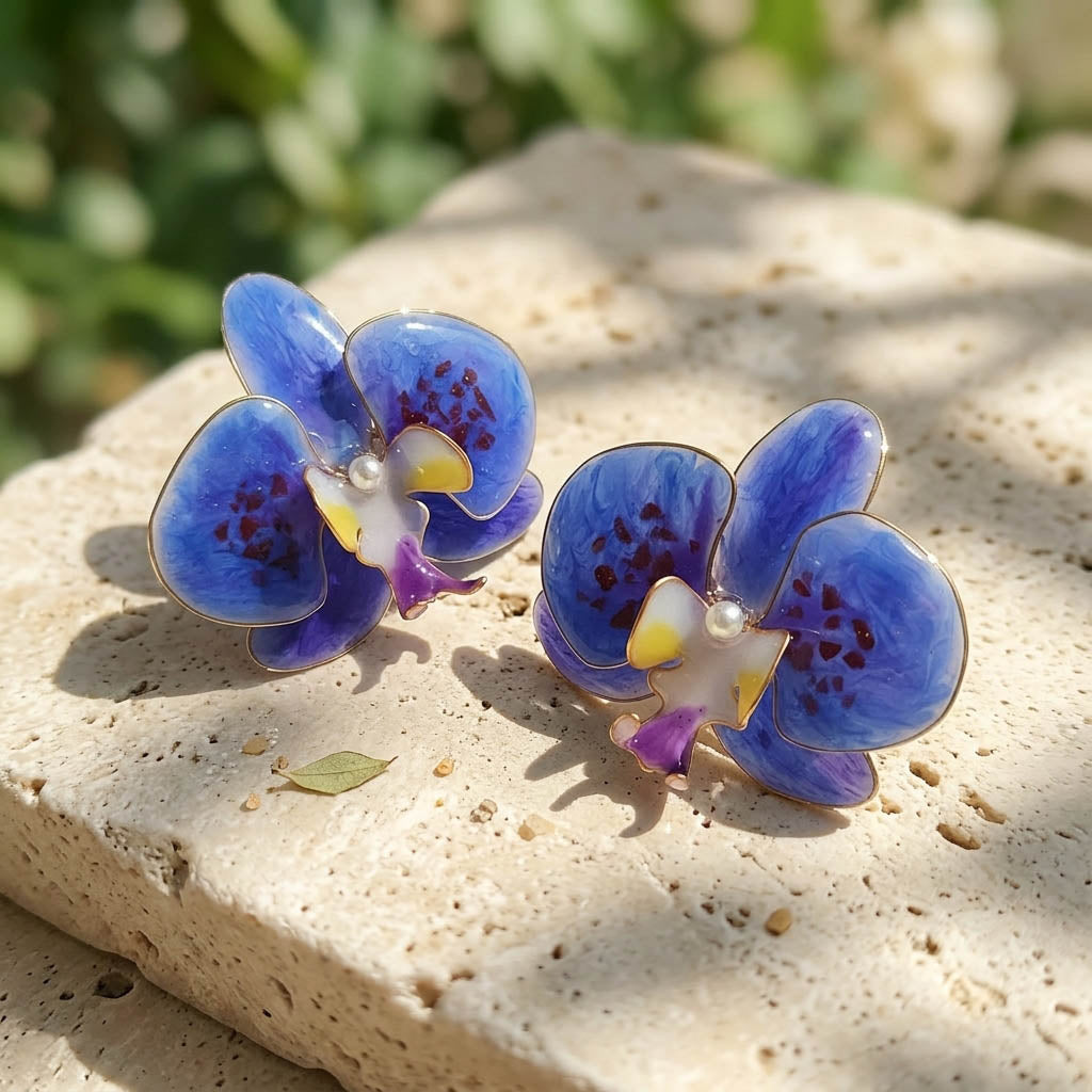 Blue orchid-shaped earrings on a stone surface with a natural background