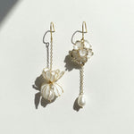 Pair of delicate earrings with floral designs and pearl-like beads on a light background