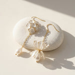 Delicate gold and pearl earrings on a white stone with soft shadows