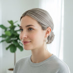 Woman with gray hair wearing earrings indoors with a plant in the background