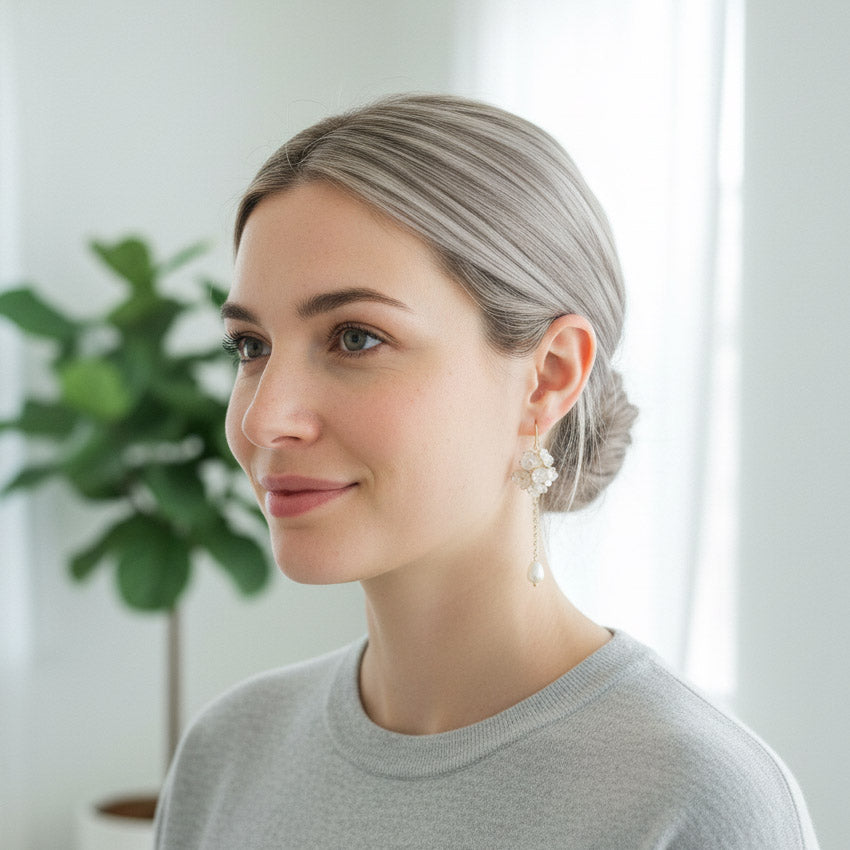 Woman with gray hair wearing earrings indoors with a plant in the background