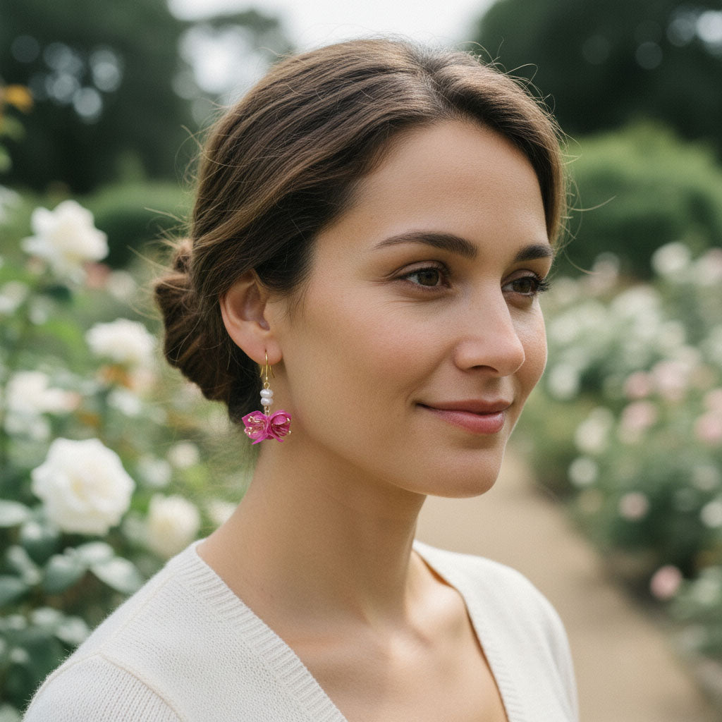 Woman with pink earrings standing in a garden with blurred flowers and greenery in the background