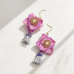 Purple floral earrings with gold centers and tassels on a white background