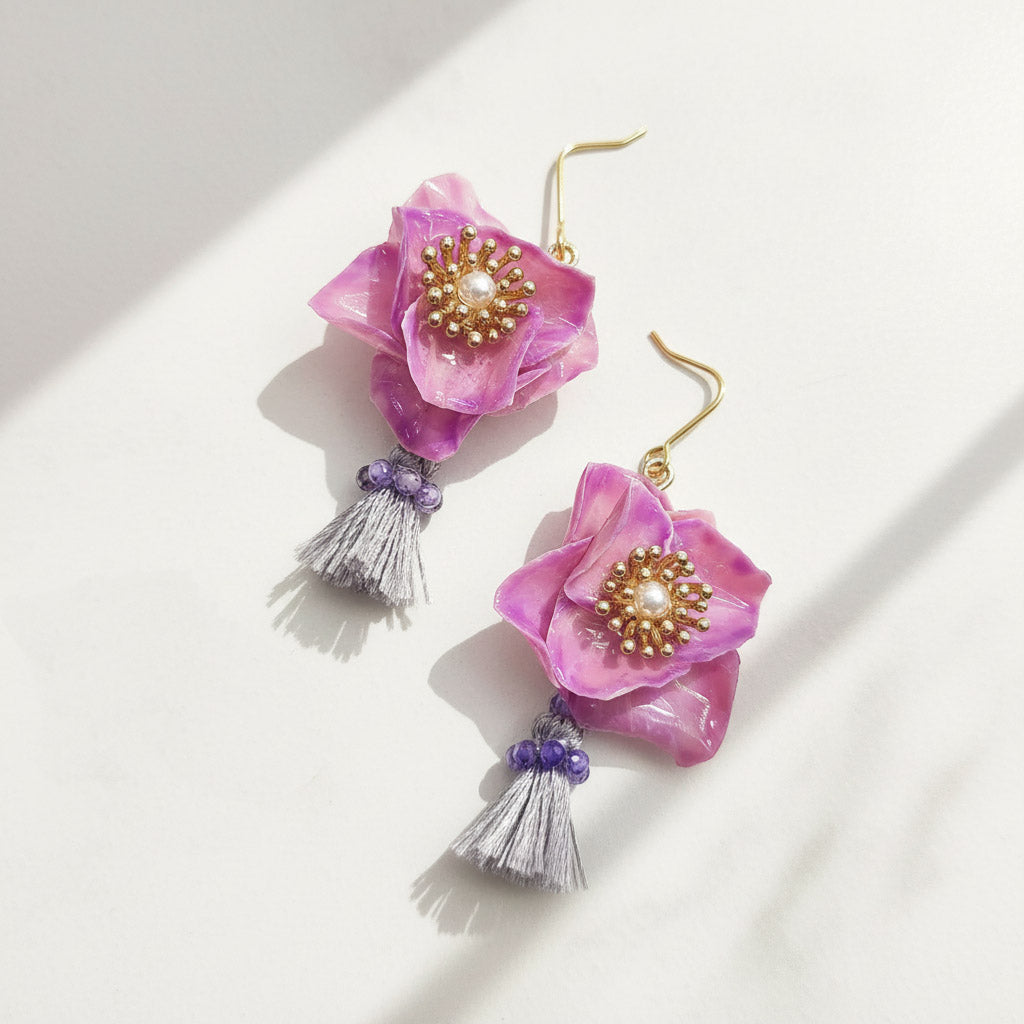 Purple floral earrings with gold centers and tassels on a white background
