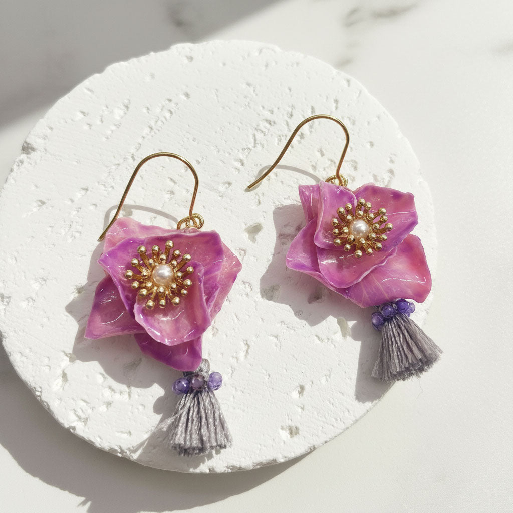 Pink flower earrings with gold centers and tassels on a white stone surface