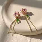 Pair of Hydrangea earrings with gold chains on a light stone surface