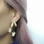 Model wearing gold-plated floral stud earrings featuring hand-carved mother-of-pearl tulip drops and freshwater pearls, highlighting their elegant dangle design against pastel pink hair.