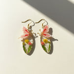 Butterfly-shaped earrings with floral elements on a light background