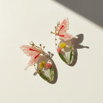 Butterfly-shaped earrings with floral details on a light background