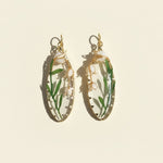 Gold hoop earrings with green leafy design on a beige background