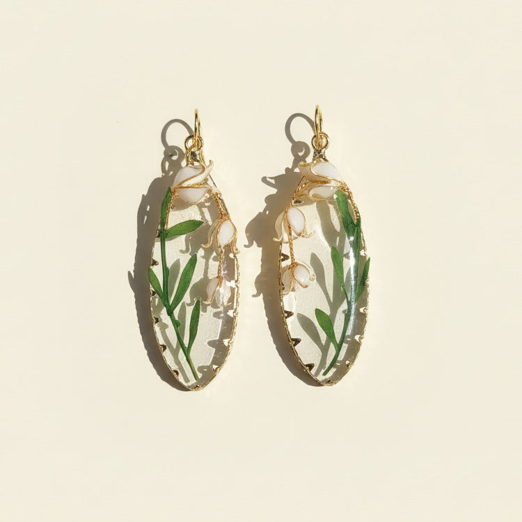 Gold hoop earrings with green leafy design on a beige background