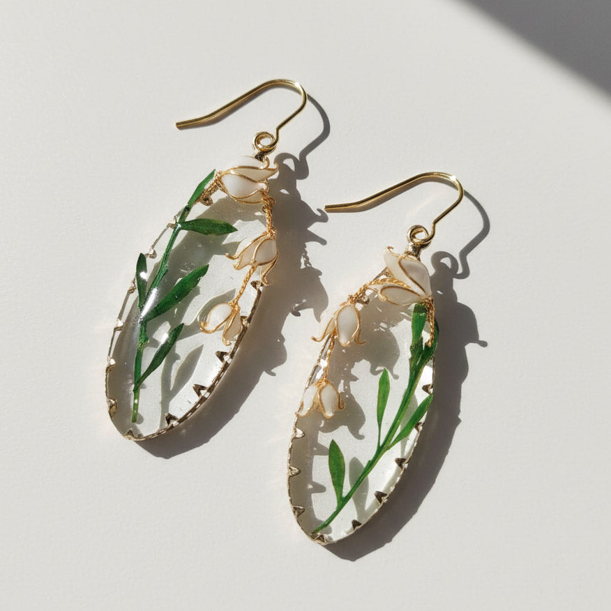 Gold earrings with green leaves and white flowers on a light background