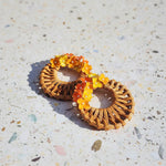 Pair of woven earrings with orange and yellow beads on a textured surface