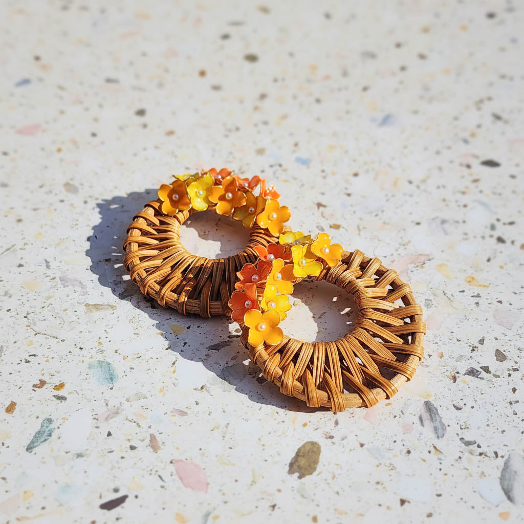 Pair of woven earrings with orange and yellow beads on a textured surface