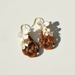 Pair of earrings with woven design and floral elements on a light background