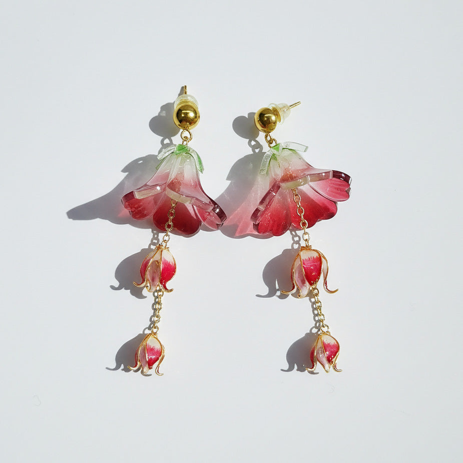 Pair of pink flower-shaped earrings with gold accents on a light gray background