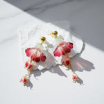Pair of floral earrings with red and gold accents on a white stone surface.
