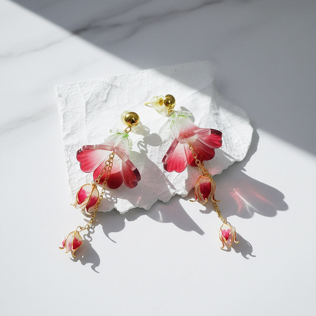 Pair of floral earrings with red and gold accents on a white stone surface.