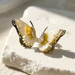 April birthstone butterfly-shaped earrings with yellow and white details on a textured surface
