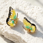 November birthstone butterfly-shaped earrings with yellow and green wings on a textured white surface