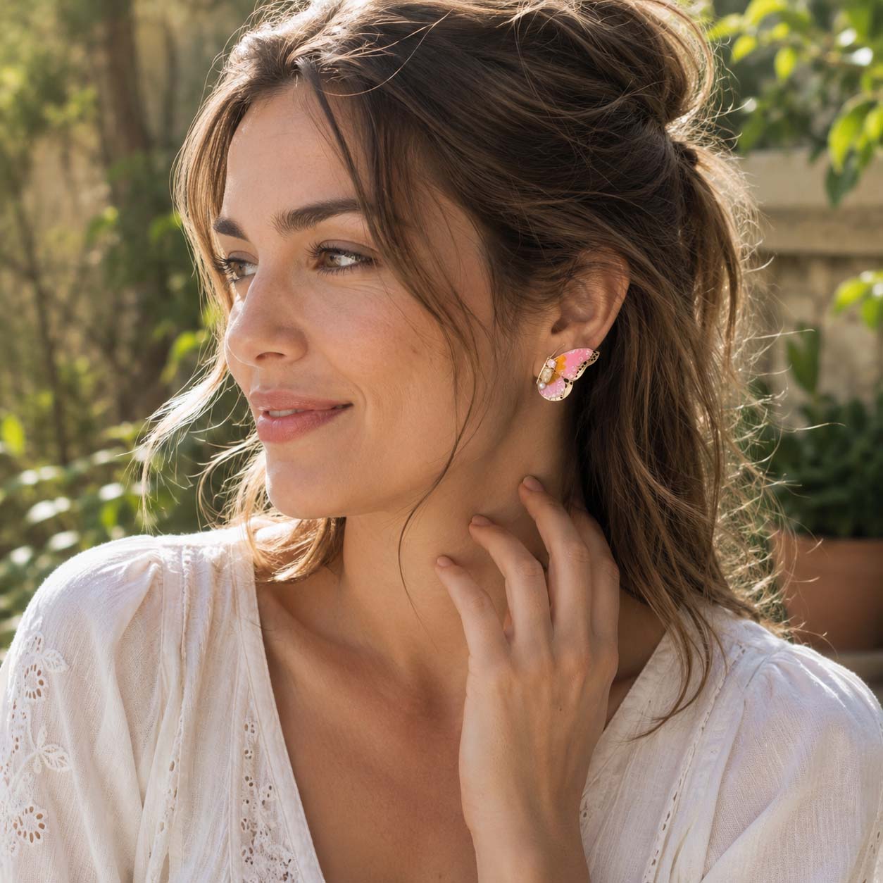Woman wearing butterfly birthstone earrings outdoors with greenery in the background