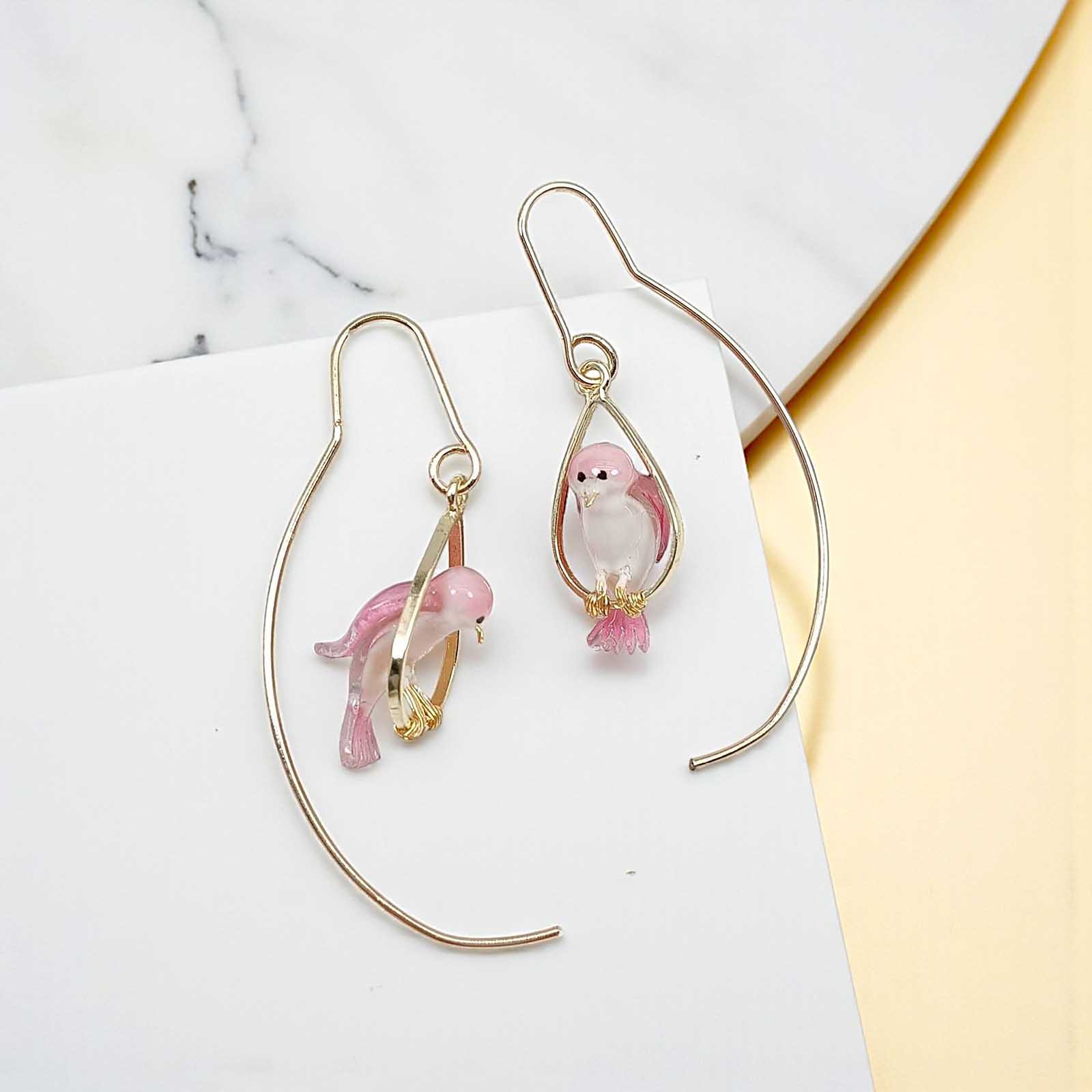 Pair of gold hoop earrings with pink fish charms on a marble surface