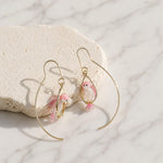 Gold hoop earrings with pink bird charms on a marble surface