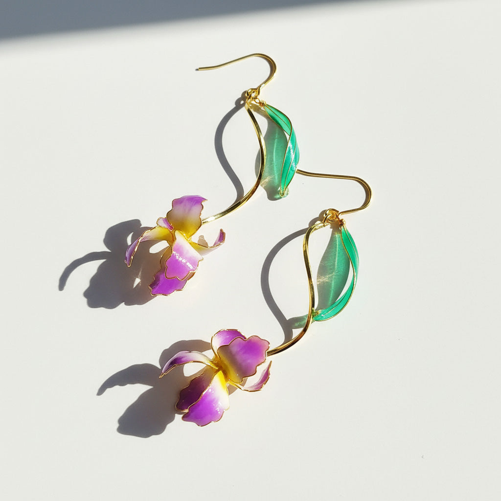 Hand-painted purple and yellow iris earrings with green leaf and gold stem on white background, sunlight and shadow.