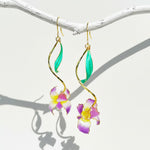 Hanging view of gold-plated iris flower earrings with green enamel leaves and soft natural shadows.