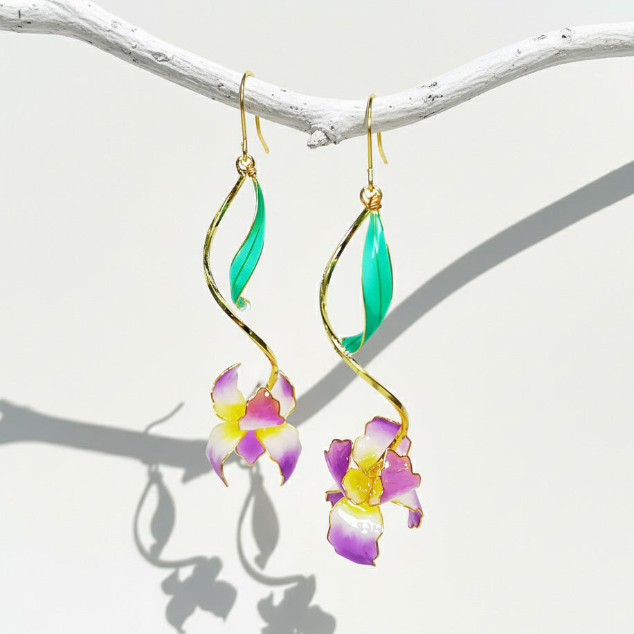 Hanging view of gold-plated iris flower earrings with green enamel leaves and soft natural shadows.