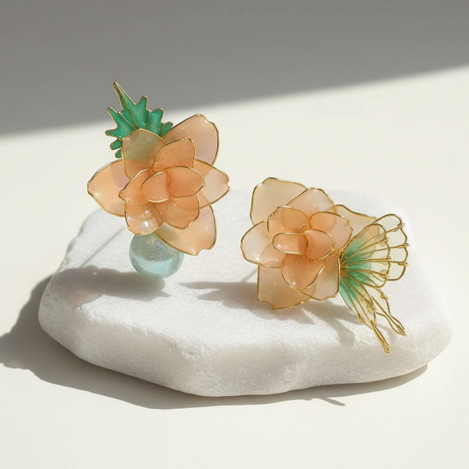 Floral earrings with green and peach colors on a white stone surface