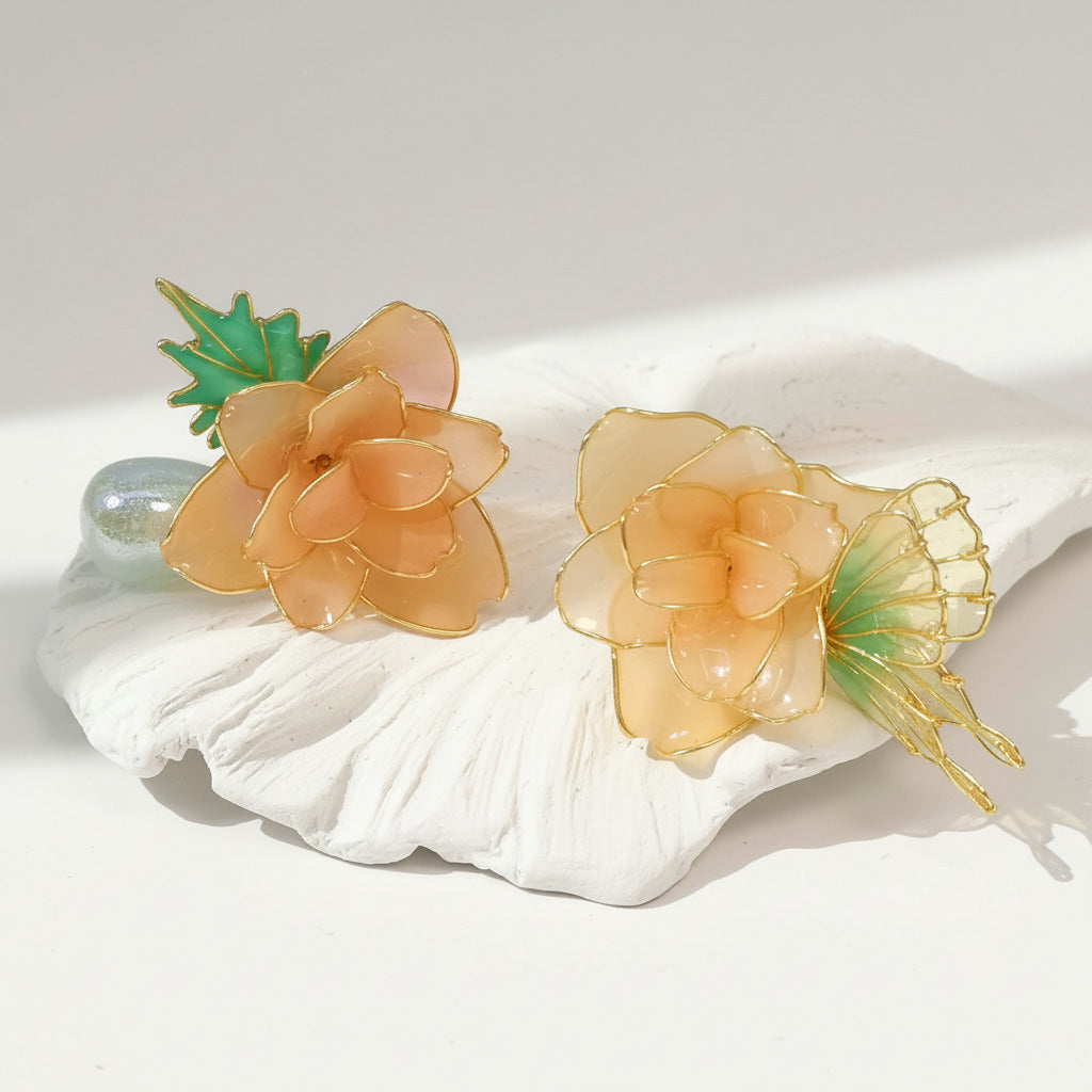 Pair of peach-colored floral earrings with green leaves on a white shell.
