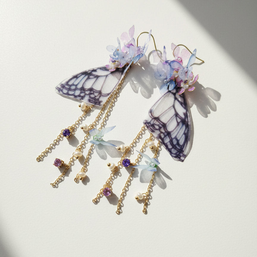 Butterfly wing and flower dangle earrings with CZ stones and pearls on white background.