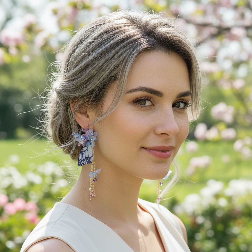 Model wearing butterfly wing dangle earrings with floral details in garden setting.