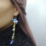 Model wearing gold-plated dangle earrings with real hydrangea flowers, hand-painted resin petals, and cascading semi-precious stone accents.