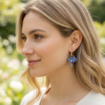 Woman wearing blue floral earrings with a blurred natural background