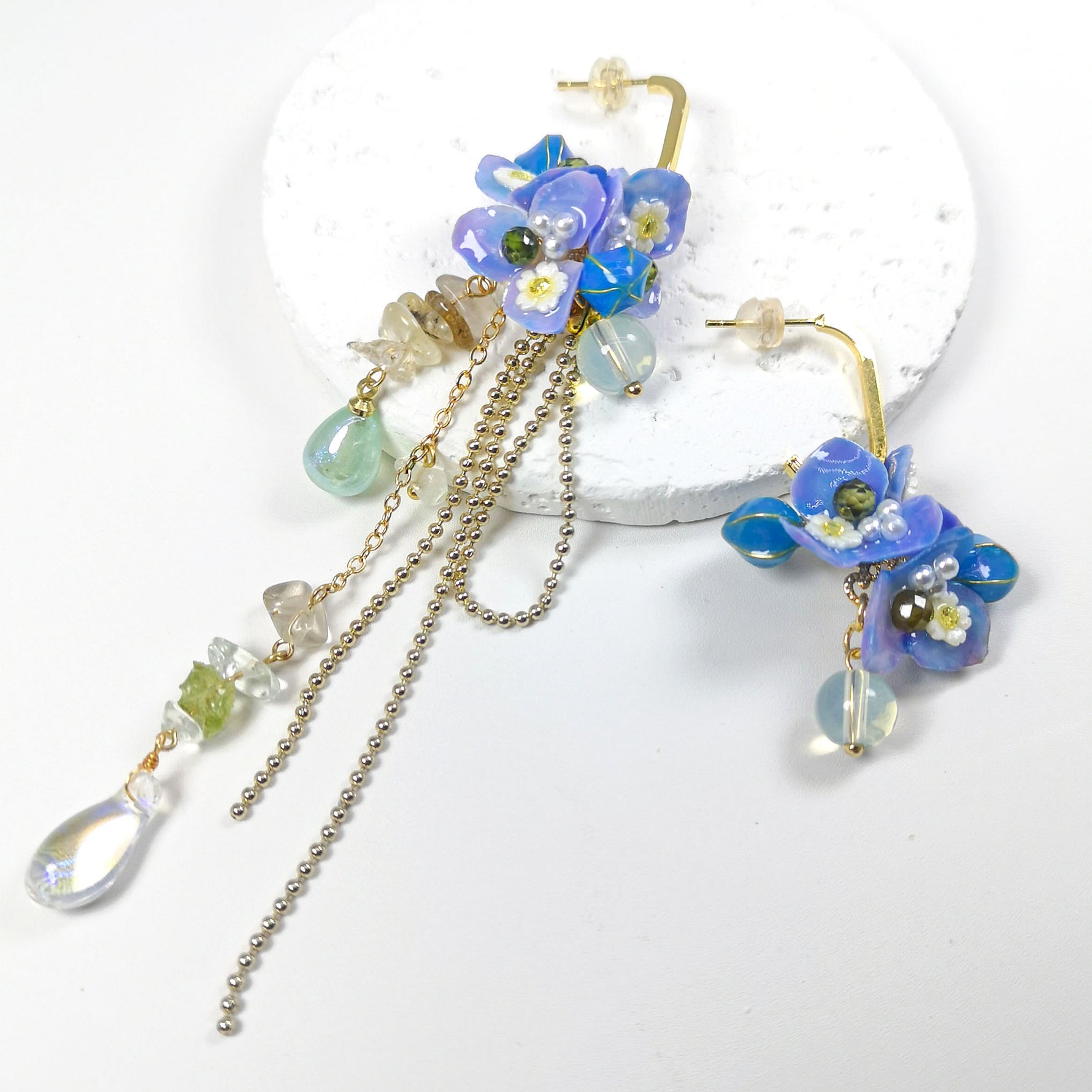 Gold-plated asymmetrical earrings with real hydrangea flowers, hand-painted resin petals, glass beads, and dangling chains adorned with semi-precious stones.