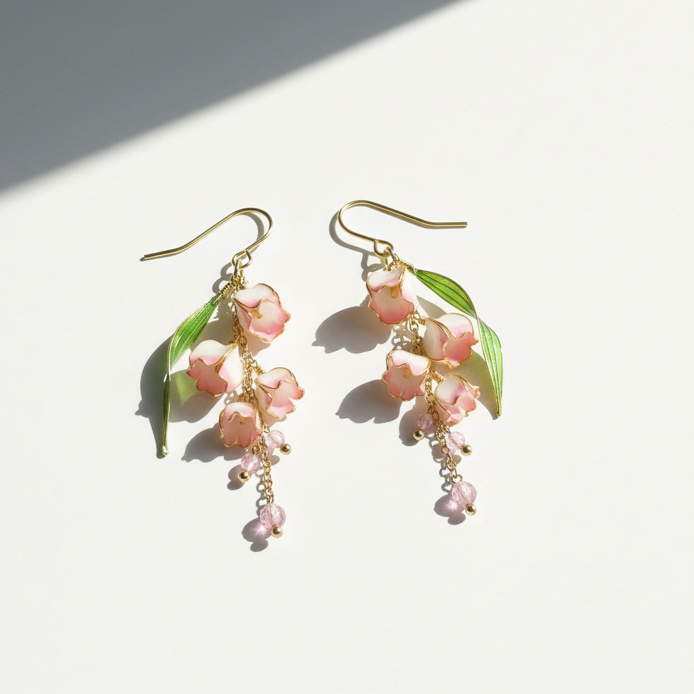 Pair of floral earrings with pink flowers and green leaves on a white background