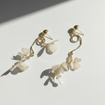 Gold earrings with white floral charms on a light background