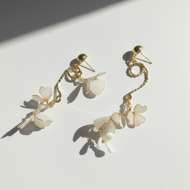 Gold earrings with white floral charms on a light background